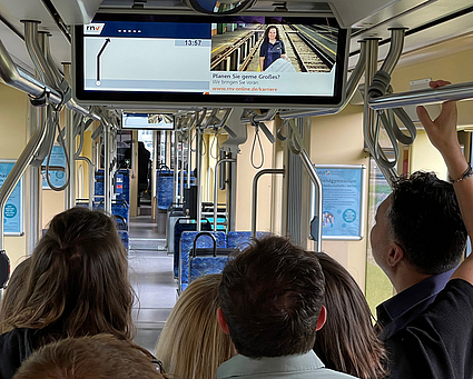 Eine Gruppe Menschen blickt auf den Fahrgast-TV-Bildschirm in einer Bahn der rnv.
