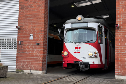 Die geöffnete Fahrzeughalle auf dem Betriebshof Käfertal. Aus dem Tor der Wagenhalle lugt die Front der Düwag-Straßenbahn Nummer 4098 vom Tyo GT8 heraus. Die Straßenbahn ist in den Farben der OEG lackiert: rot und weiß.