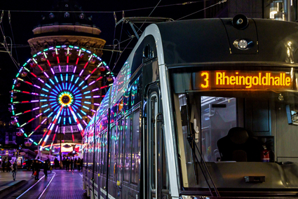 Eine Rhein-Neckar-Tram (RNT) der Linie 3 mit dem Ziel ‚Rheingoldhalle‘ steht nachts vor dem Mannheimer Wasserturm. Hinter ihr leuchtet ein großes, bunt beleuchtetes Riesenrad.