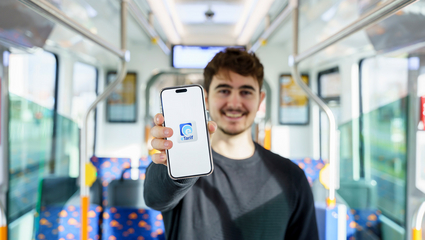 Ein Mann steht in einer Straßenbahn der rnv und hält ein Smartphone mit dem Logo der rnv-eTarif-App in die Kamera.