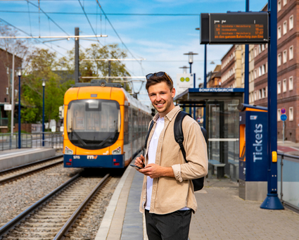 Junger Mann mit Smartphone an einer Stadtbahnhaltestelle