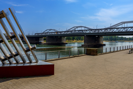 An der Ludwigshafener Rheinpromenade: Blick auf den Rhein und die Konrad-Adenauer-Brücke bei blauem Himmel, Sonnenschein und ein paar ganz kleinen Schleierwolken. Auf der Brücke fährt eine Stadtbahn des Typs "Rhein-Neckar-Tram" (RNT).