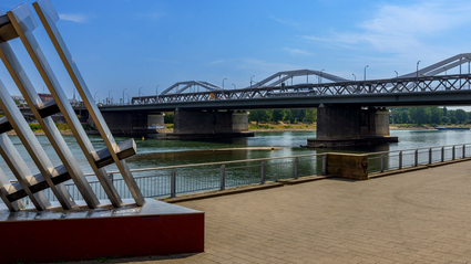 An der Ludwigshafener Rheinpromenade: Blick auf den Rhein und die Konrad-Adenauer-Brücke bei blauem Himmel, Sonnenschein und ein paar ganz kleinen Schleierwolken. Auf der Brücke fährt eine Stadtbahn des Typs "Rhein-Neckar-Tram" (RNT).