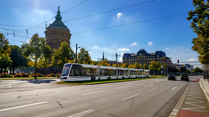 Eine rnv-Stadtbahn des Typs Rhein-Neckar-Tram (RNT) fährt an einem sonnigen Frühlingstag auf dem Kaiserring bzw. Friedrichsring in Mannheim von der Haltestelle Kunsthalle in Richtung der Haltestelle Rosengarten. Im Hintergrund der Mannheimer Wasserturm.