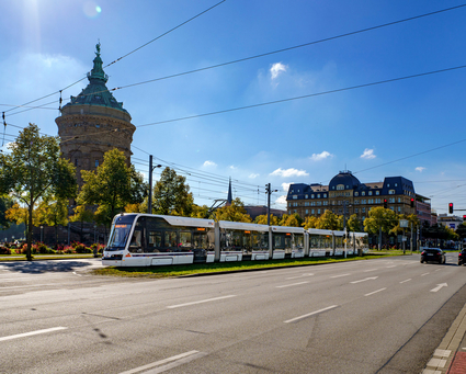 Eine rnv-Stadtbahn des Typs Rhein-Neckar-Tram (RNT) fährt an einem sonnigen Frühlingstag auf dem Kaiserring bzw. Friedrichsring in Mannheim von der Haltestelle Kunsthalle in Richtung der Haltestelle Rosengarten. Im Hintergrund der Mannheimer Wasserturm.