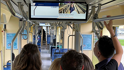Eine Gruppe Menschen blickt auf den Fahrgast-TV-Bildschirm in einer Bahn der rnv.