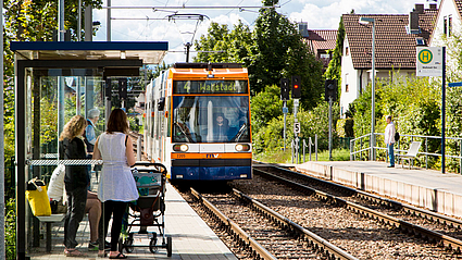 Fahrgäste mit Kinderwagen warten an einer Haltestelle auf die Straßenbahn.