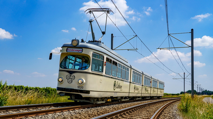 Die Event-Bahn "RHB-1020" des Typs DÜWAG auf der Strecke vor blauem Himmel mit ein paar Wölkchen.