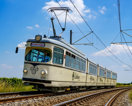 Die Event-Bahn "RHB-1020" des Typs DÜWAG auf der Strecke vor blauem Himmel mit ein paar Wölkchen.