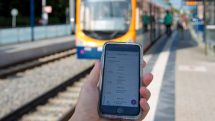 Hand hält Handy mit eTarif-App an einer Stadtbahnhaltestelle